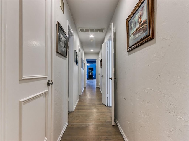 hall with wood finished floors, a textured wall, visible vents, and baseboards