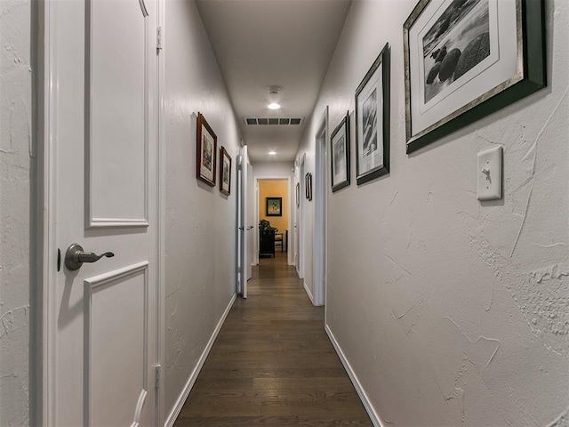 corridor featuring a textured wall, baseboards, visible vents, and dark wood-style flooring