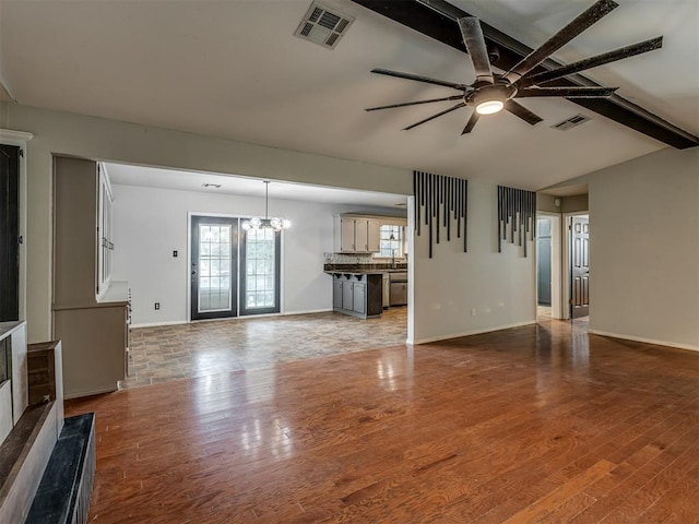 unfurnished living room with ceiling fan with notable chandelier, light wood finished floors, visible vents, and baseboards