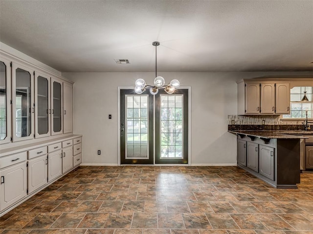 kitchen with glass insert cabinets, visible vents, a notable chandelier, and baseboards