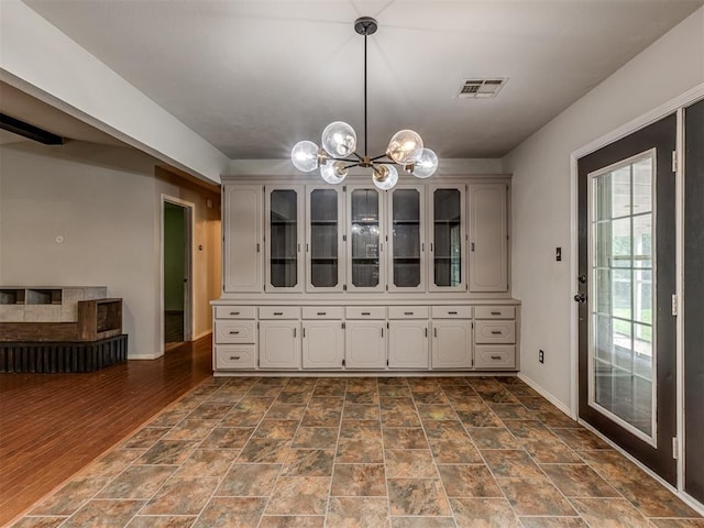 kitchen featuring a notable chandelier, visible vents, hanging light fixtures, glass insert cabinets, and baseboards