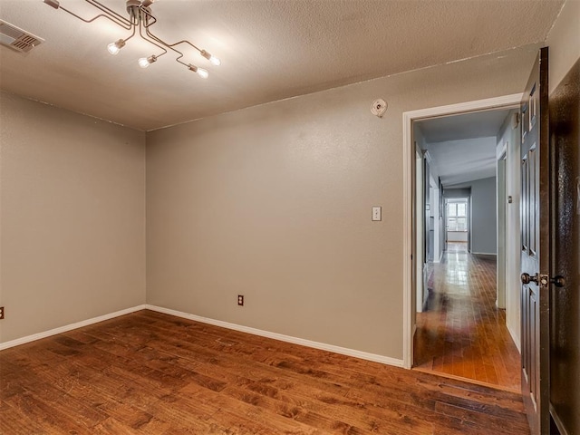 spare room with visible vents, a textured ceiling, baseboards, and wood finished floors