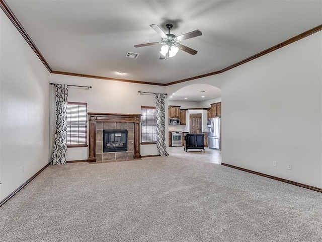 unfurnished living room featuring baseboards, visible vents, arched walkways, a tile fireplace, and light colored carpet