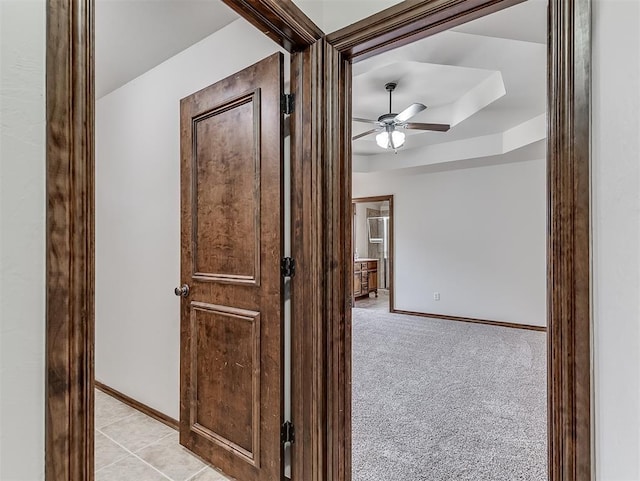 hall with baseboards, a raised ceiling, and light colored carpet