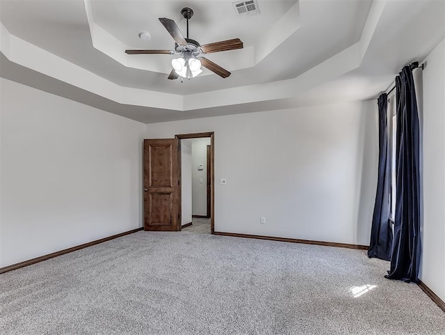 spare room with a tray ceiling, visible vents, light carpet, and baseboards