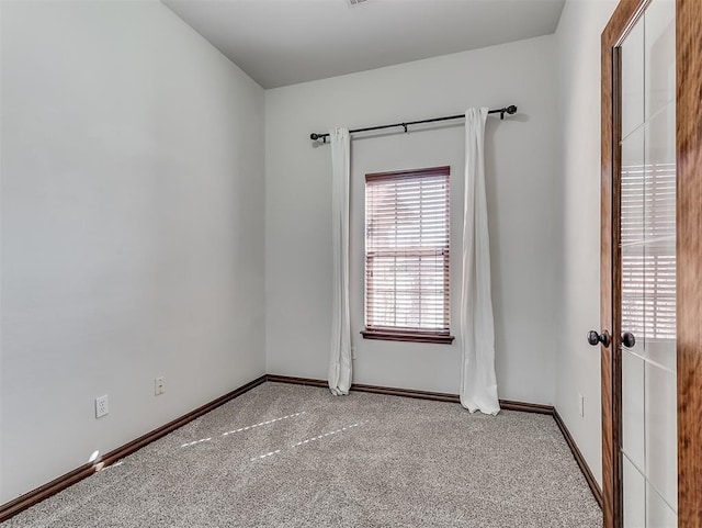 spare room featuring light colored carpet and baseboards