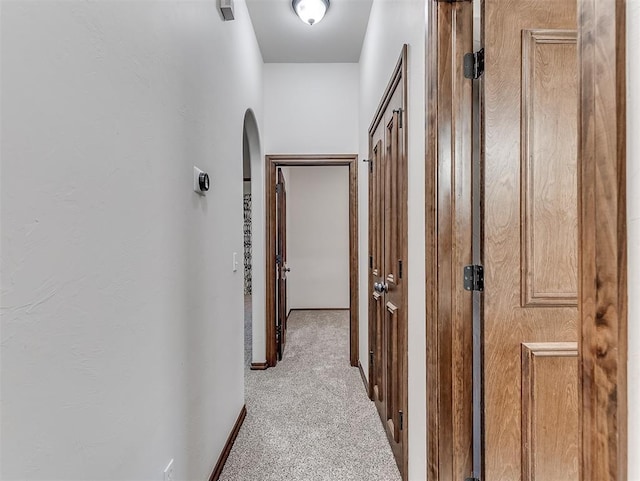 hallway with arched walkways and light colored carpet