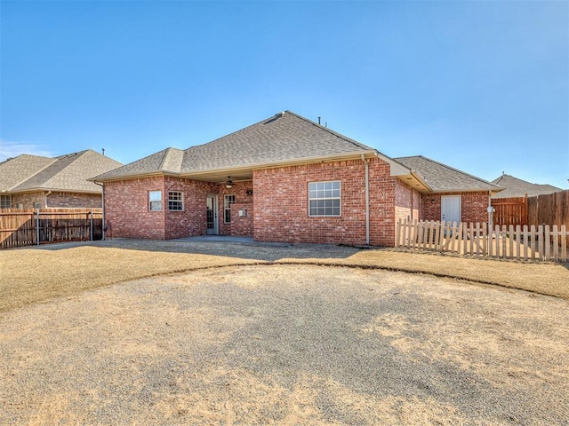 back of house with a fenced backyard, brick siding, and roof with shingles