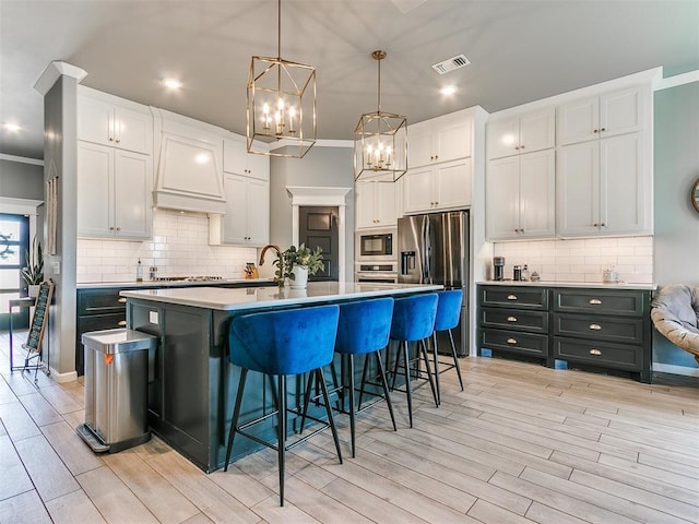 kitchen featuring white cabinets, a kitchen island with sink, visible vents, and stainless steel appliances