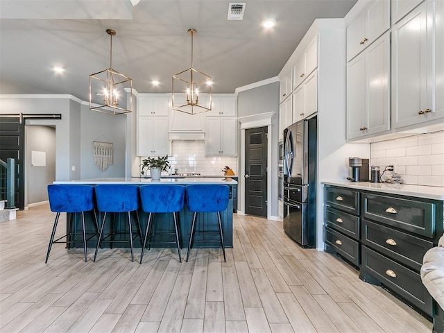 kitchen with visible vents, a barn door, freestanding refrigerator, white cabinetry, and a kitchen island