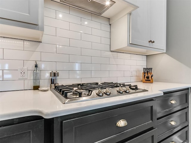 kitchen with light countertops, tasteful backsplash, range hood, and stainless steel gas stovetop