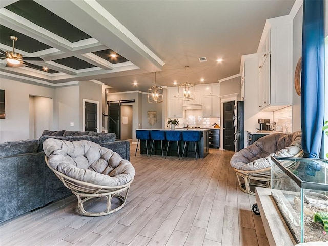 interior space with a barn door, ceiling fan with notable chandelier, coffered ceiling, light wood-type flooring, and crown molding