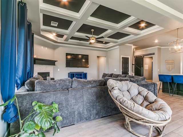 living area with a barn door, ceiling fan with notable chandelier, a fireplace, coffered ceiling, and visible vents