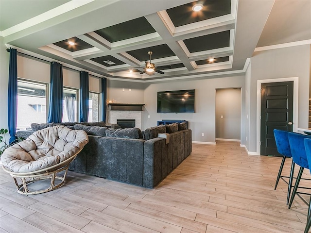 living area with a fireplace, coffered ceiling, a ceiling fan, baseboards, and light wood finished floors