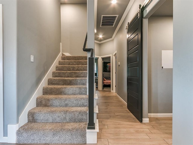 staircase with visible vents, a barn door, ornamental molding, wood finished floors, and baseboards