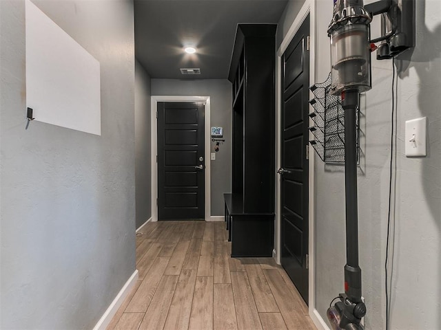 hall with light wood-type flooring, baseboards, and visible vents