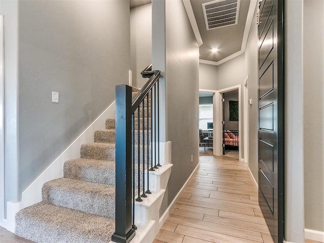 stairs featuring baseboards, wood finished floors, visible vents, and crown molding