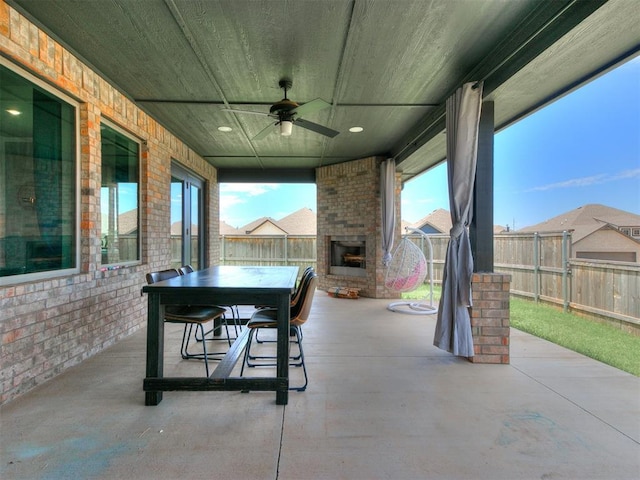 view of patio / terrace with an outdoor brick fireplace, outdoor dining area, a fenced backyard, and ceiling fan