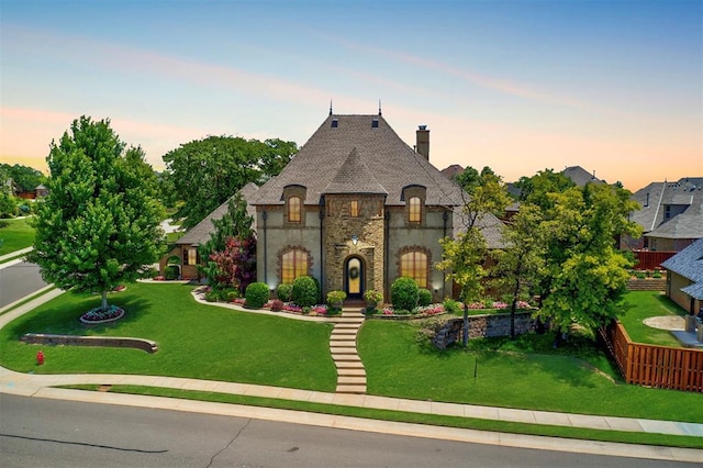 french country style house featuring a front lawn, stone siding, and a chimney