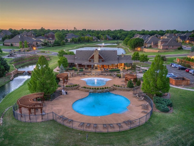 pool at dusk with a patio area, a residential view, fence, and a water view