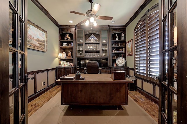 home office featuring built in features, a ceiling fan, ornamental molding, wainscoting, and a decorative wall