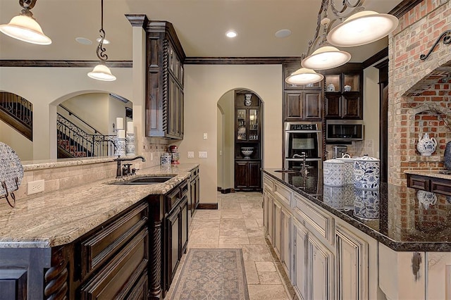 kitchen featuring a sink, stone tile floors, arched walkways, appliances with stainless steel finishes, and dark brown cabinets