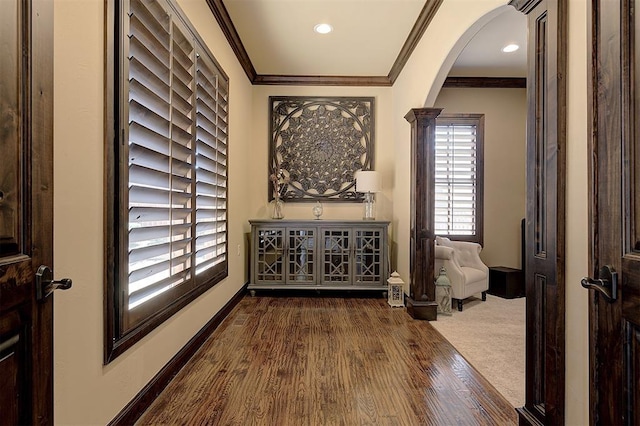 hallway featuring crown molding, baseboards, decorative columns, arched walkways, and dark wood-style flooring