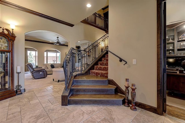 stairs with ornamental molding, stone tile flooring, arched walkways, baseboards, and ceiling fan