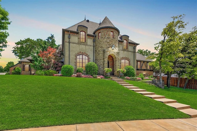 french country home with stone siding, a yard, and fence