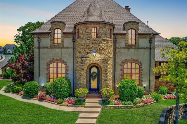 french country style house with a chimney, a front yard, and roof with shingles