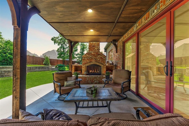 patio terrace at dusk featuring an outdoor living space with a fireplace and fence