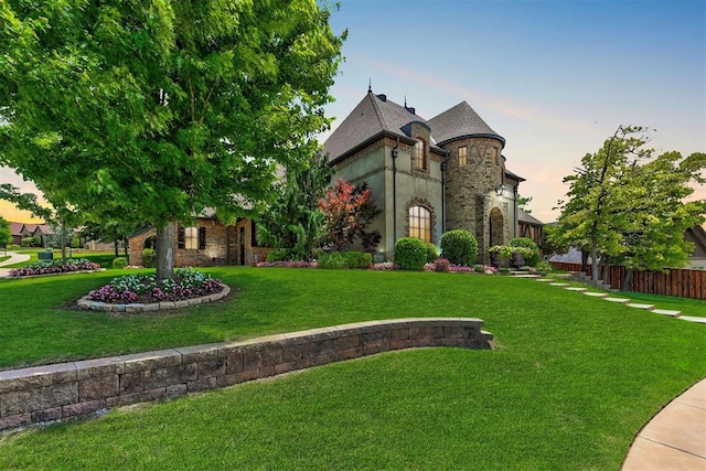 french country style house featuring a yard, stone siding, and fence