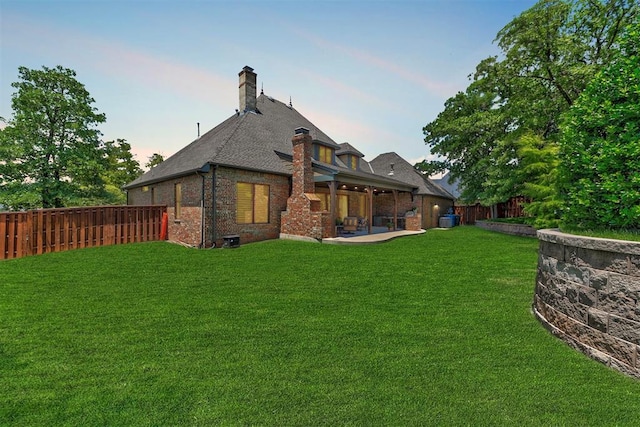 rear view of house featuring a yard, brick siding, a chimney, and a patio area