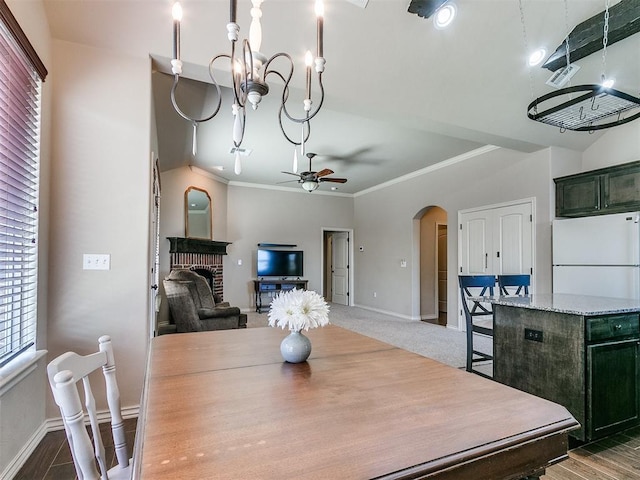 dining room featuring baseboards, arched walkways, ornamental molding, a brick fireplace, and ceiling fan with notable chandelier