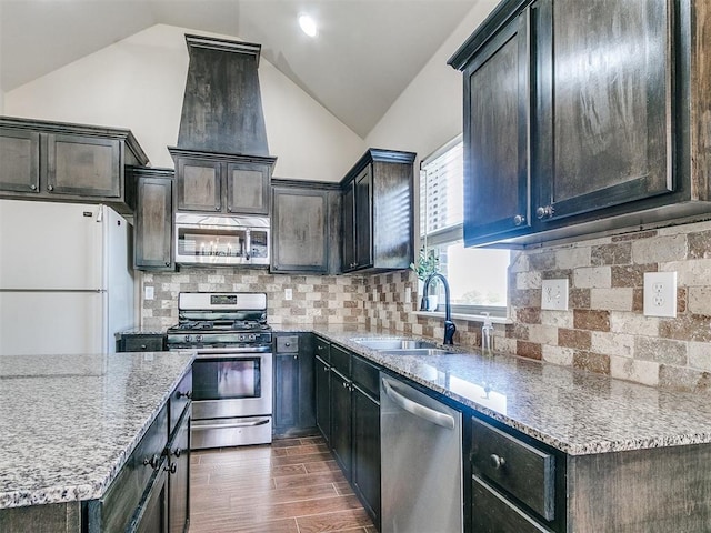 kitchen featuring lofted ceiling, light stone counters, stainless steel appliances, a sink, and decorative backsplash