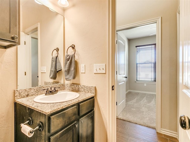 bathroom featuring a textured wall, baseboards, wood finished floors, and vanity