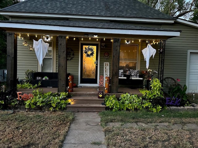 view of exterior entry with covered porch and a shingled roof