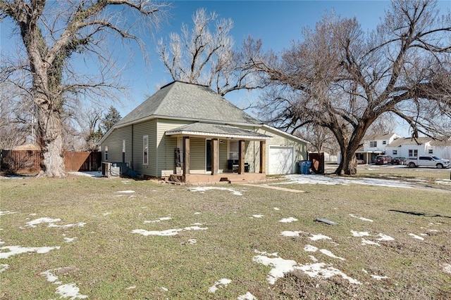 view of front of house featuring roof with shingles, an attached garage, covered porch, fence, and a front yard