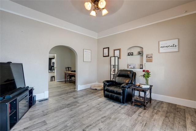 living area with light wood-type flooring, arched walkways, ceiling fan, and baseboards