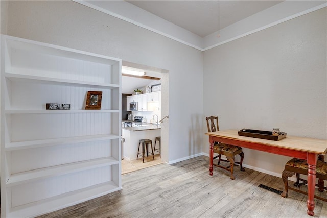 home office featuring light wood-style floors, visible vents, baseboards, and vaulted ceiling