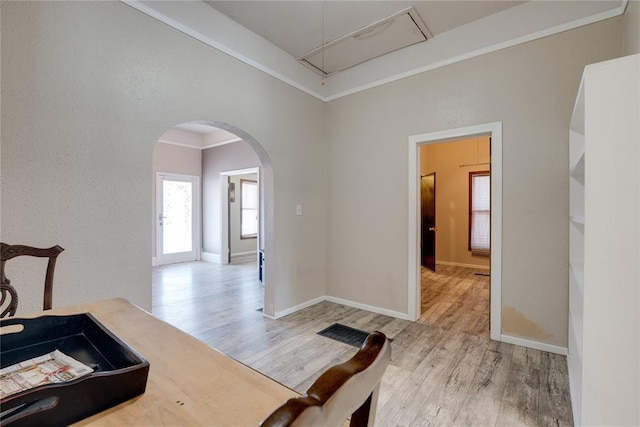 dining space featuring arched walkways, crown molding, light wood-style floors, attic access, and baseboards