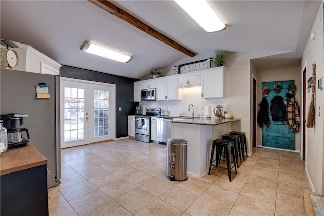 kitchen featuring lofted ceiling with beams, stainless steel appliances, french doors, white cabinetry, and a sink