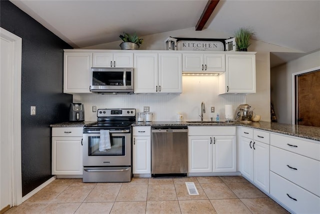 kitchen with light tile patterned floors, dark stone countertops, vaulted ceiling with beams, stainless steel appliances, and white cabinetry