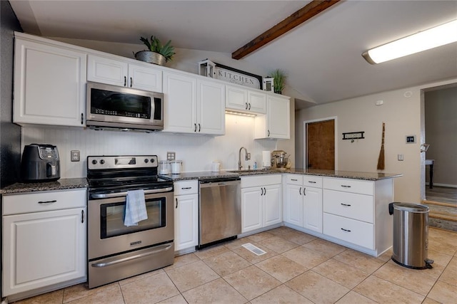 kitchen with vaulted ceiling with beams, stainless steel appliances, a peninsula, white cabinetry, and dark stone countertops