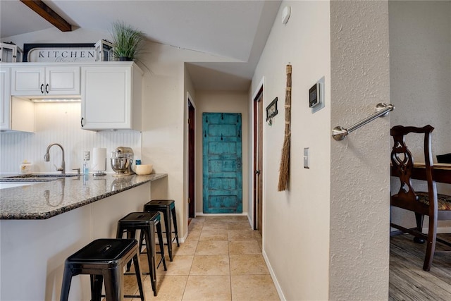 kitchen featuring a breakfast bar area, white cabinets, a sink, and dark stone counters