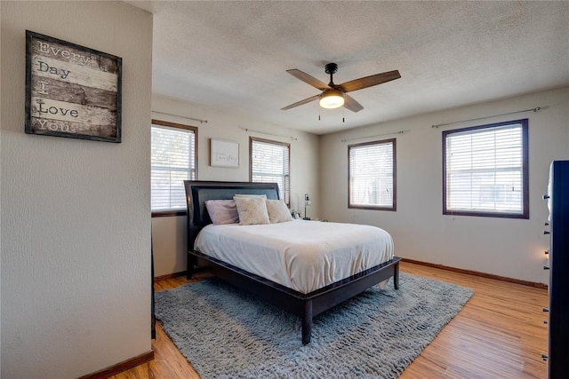 bedroom with baseboards, multiple windows, light wood-style flooring, and a textured ceiling