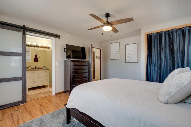 bedroom with a barn door, a ceiling fan, ensuite bathroom, light wood-style floors, and a sink