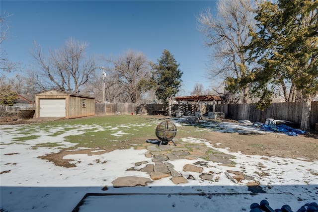 yard layered in snow with an outdoor fire pit, a fenced backyard, a detached garage, and an outbuilding