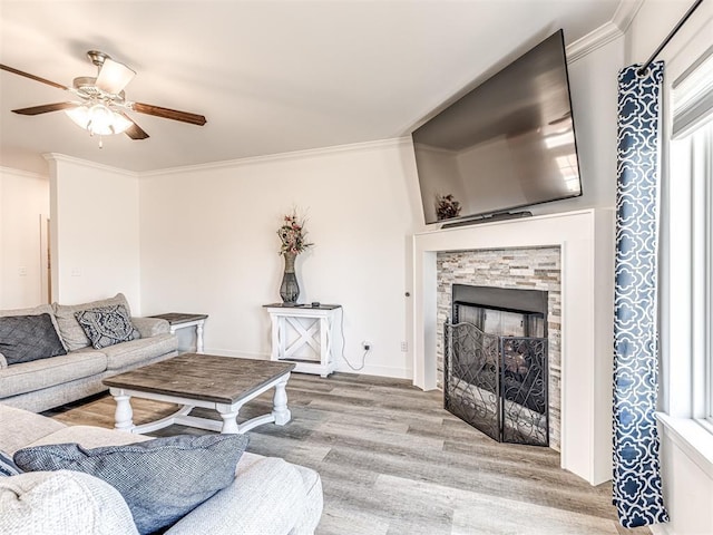 living area featuring light wood-type flooring, a fireplace, a ceiling fan, and crown molding