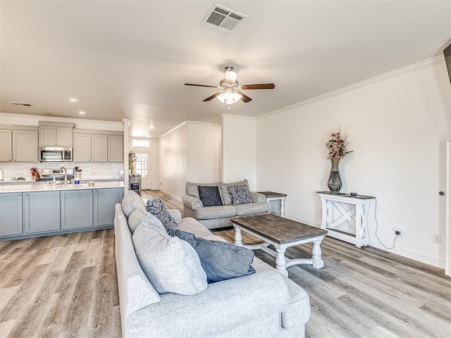 living room featuring light wood-style floors, visible vents, and crown molding